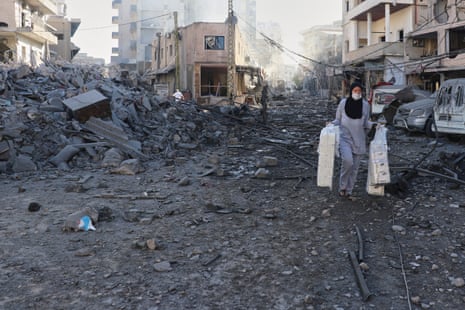 A woman carrying items as she walks away from a destroyed building.