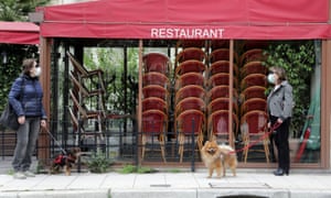 two women and their dogs stand outside a closed cafe with stacked chairs