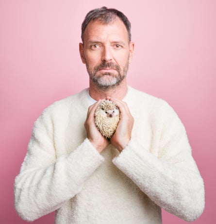 Tim Dowling holding a baby hedgehog between cupped hands, against pink backgroubd