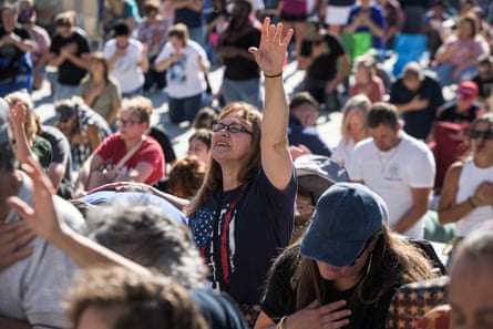 Crowd of people, with women in center raising hand in praise and wearing a US flag T-shirt.