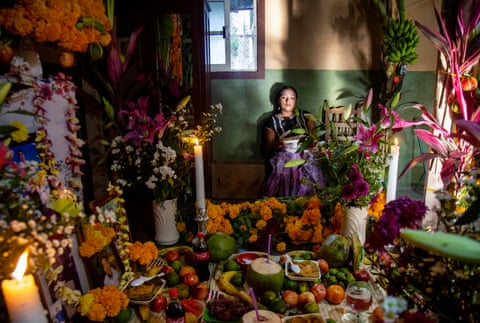 A woman sits as she looks at a table filled with flowers, fruits and candles