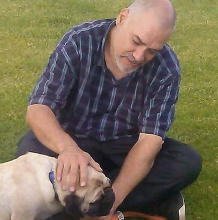 man wearing checkered shirt and sitting on grass pets a dog