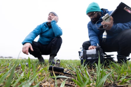 Two men crouch in a field with recording equipment
