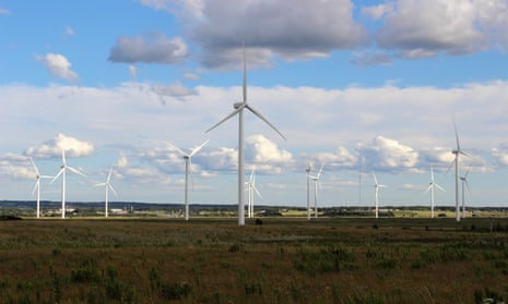 white windmills standing tall in a green field with blue sky splattered with tufts of clouds
