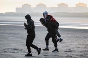 A man carries a woman on his back as they prepare to embark on the beach of Gravelines
