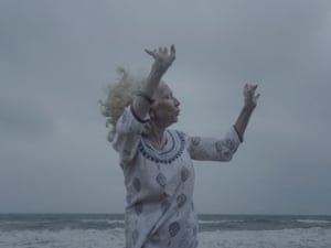 A blue-grey toned image of an albino Indian woman raising her hands against the sea