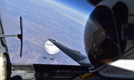 Pilot wearing helmet with spy balloon visible through window of jet.