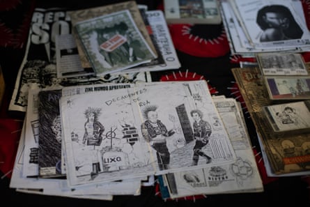 A spread of black-and-white zines and pamphlets with hand-drawn illustrations and punk-style graphics laid out on a surface, with some colour prints and photographs mixed in.