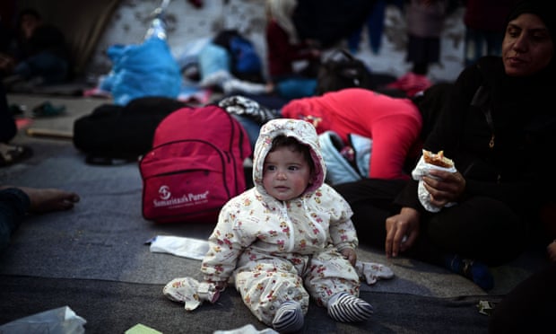 A baby sits on a blanket near his mother in the port in the town of Chios