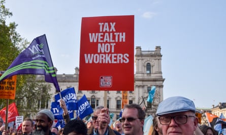 A protest march at which a placard reads ‘Tax wealth not workers’