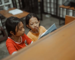 two children reading a book together in library