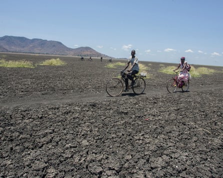 Two people cycle over the dried and cracked lake bed