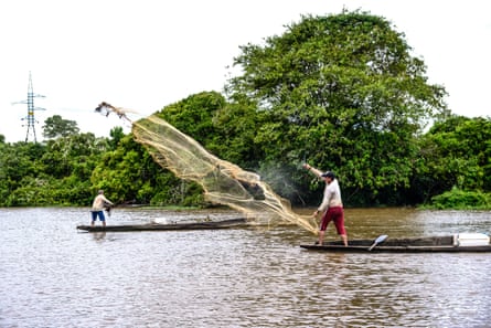 Two men standing in little pirogue-type boats cast nets over still inland waters