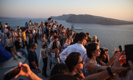 People stand on an outcrop at sunset with the sea and an island in the background.