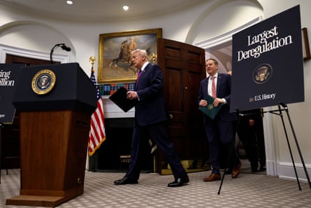 two men in suits enter a room near a sign that says ‘largest deregulation in US history’