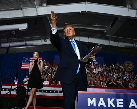 Donald Trump raises his arm, throwing a pen into a cheering rally crowd