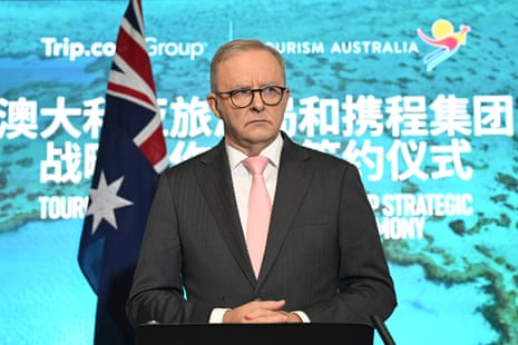 A man in a dark suit and pink tie speaks.