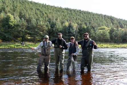Big Zuu & AJ Tracey posing the cameras in a river with fly fishing gear, alongside two fly fishers.
