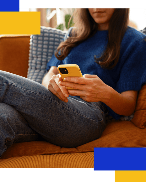 A woman relaxes on an orange couch, looking at a yellow phone in her hands
