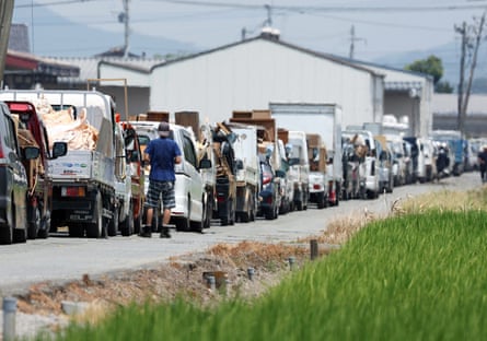 Vehicles wait in line to transport disaster debris to a temporary storage site in Hikawa, amid sweltering temperatures.