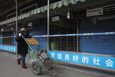 a woman wears a mask while pushing a wheelbarrow past the closed Huanan Seafood Wholesale Market