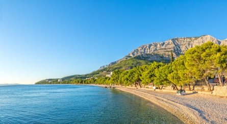 Sunny sea beach and trees in Croatia with rocky outcrop in distance
