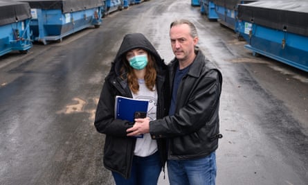 A couple standing on the a road lined by big, blue containers covered with black tarp.