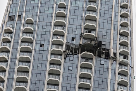 A close-up shot shows a lot of balconies and windows of a tall residential building. The middle of the building is missing its side and looks as if its walls had been blown off.