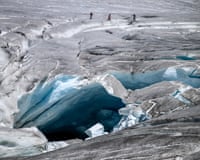 group of hikers make their way past a melt hole on the melting Rhône Glacier, above Gletsch in the Swiss Alps