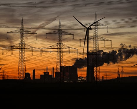 GERMANY-INDUSTRY-ENERGY-ELECTRICITY-WIND-COAL-RWEThis picture taken at sunset on November 12, 2025 shows wind turbines and power poles as fumes rise from the cooling towers of the lignite-fired power station operated by German energy giant RWE near Neurath, western Germany. (Photo by Ina FASSBENDER / AFP) (Photo by INA FASSBENDER/AFP via Getty Images)
