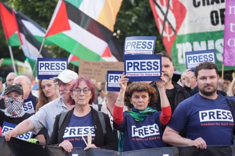 Protesters hold “press” signs and Palestine flags at a demonstration.