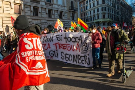 A protestors draped in a banner, in front of a crowd of marchers carrying another banner