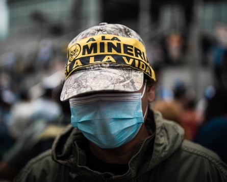 A man wearing a blue surgical mask and a cap with a yellow and black slogan in Spanish taped across it.