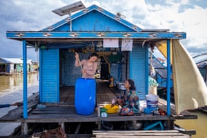 Kem Rai uses a long stick to stir liquid in a blue plastic barrel on the porch of a blue-painted floating house