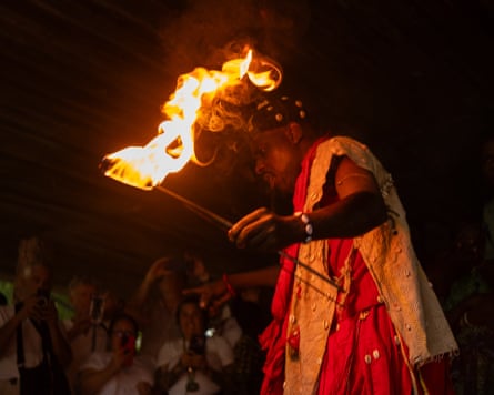 A man in traditional dress with cowrie shells sewn on it holding a burning torch