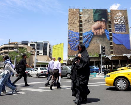A woman crosses a street in Tehran near a government billboard depicting the strait of Hormuz with a caption reading: ‘Forever in Iran’s Hand’.