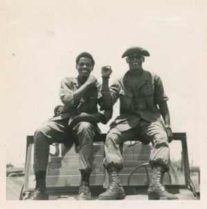 Two soldiers, in military fatigues, sitting on the edge of a jeep’s windshield in Vietnam in 1967, holding their fists in the air when Black Power salutes were prohibited the military