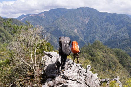 Two people carrying large backpacks hike across a rocky outcrop.