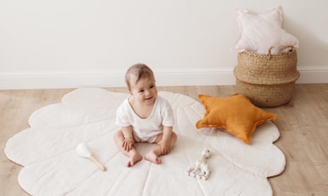 Smiling toddler sitting on shell rug with eco toys, star pillows and a basket on the wooden floor