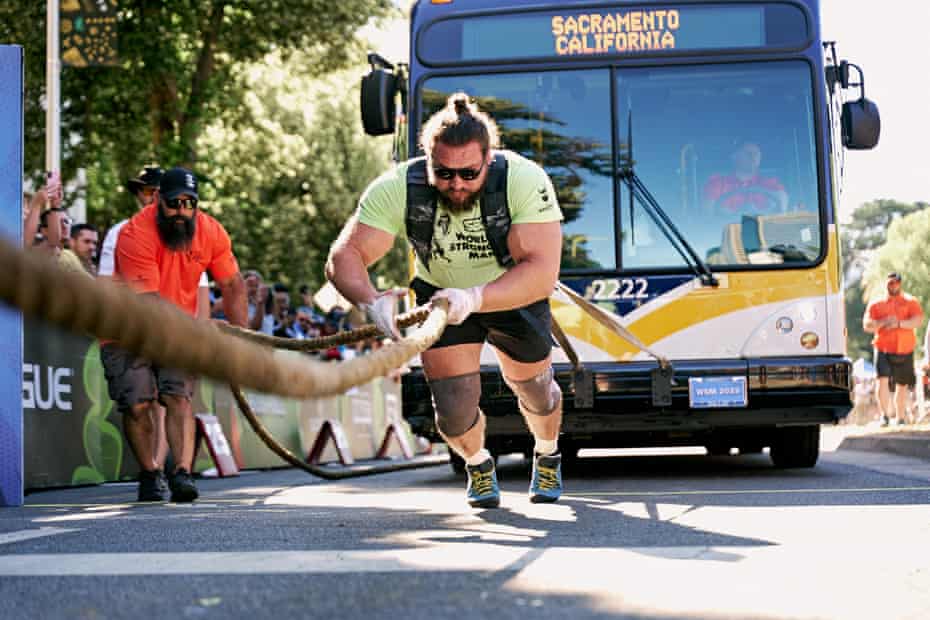 large man pulls rope with bus behind him
