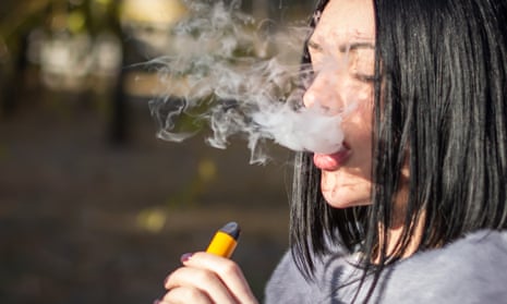 The girl smokes an electronic cigarette on the street. Vaping teenager