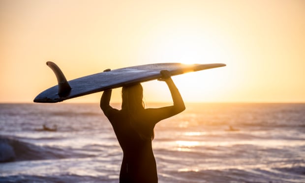 female surfer at sunrise standing on beach
