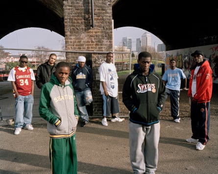 Tinchy Stryder & Ruff Sqwad stand in various positions in front of some railway arches, the Canary Wharf financial complex in the back.