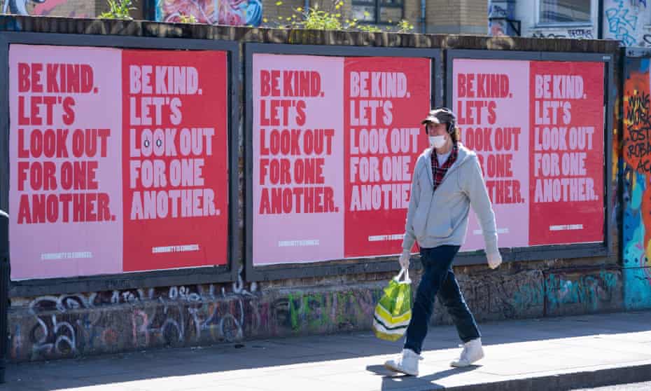 A man wearing a face mask passes a row of posters in Shoreditch, east London