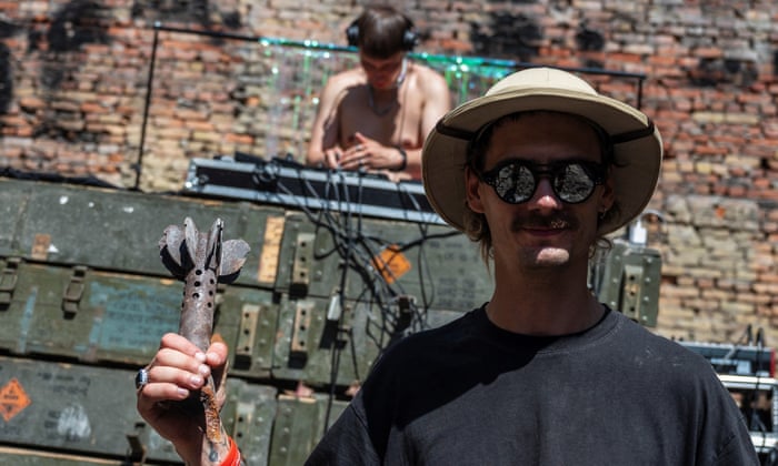 A volunteer poses for a picture with a part of a mortar shell while DJ performs in the House of a Culture in the village of Yahidne, Chernihiv.
