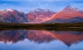 An Teallach, with a sharp peak and a range of other mountains, at sunrise with a lake in front of it