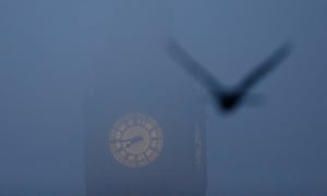 A bird flies past the Big Ben clock tower on a foggy morning in central London