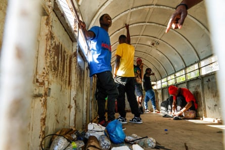 Five men stand inside the back of a white immigration truck. The floor is strewn with rubbish