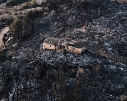 A wide view of a lone building surrounded by scorched earth after the wildfire in Bédar