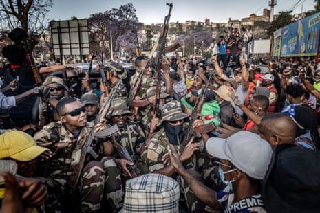 Men in camouflage holding guns ride on a pickup truck surrounded by protesters